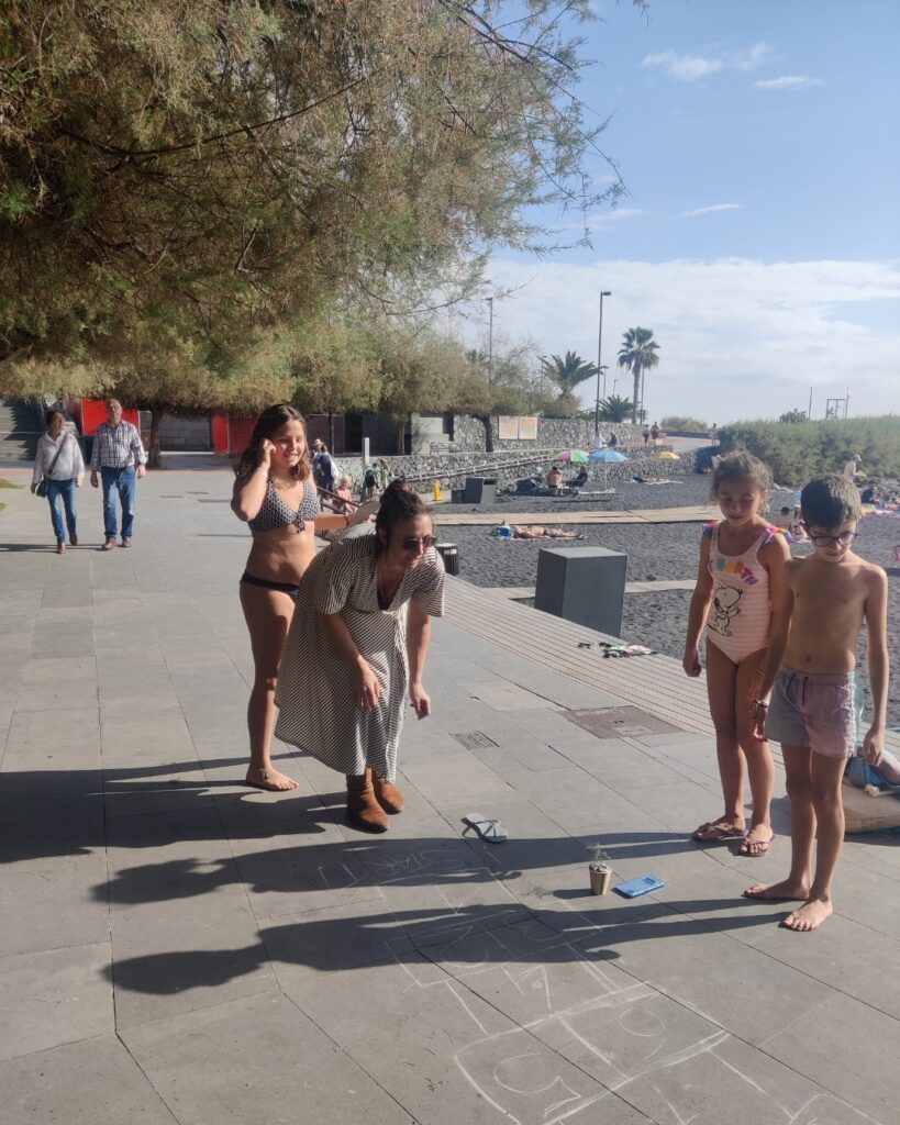 Kinder spielen mit einer Frau ein Hüpfspiel an einer Uferpromenade